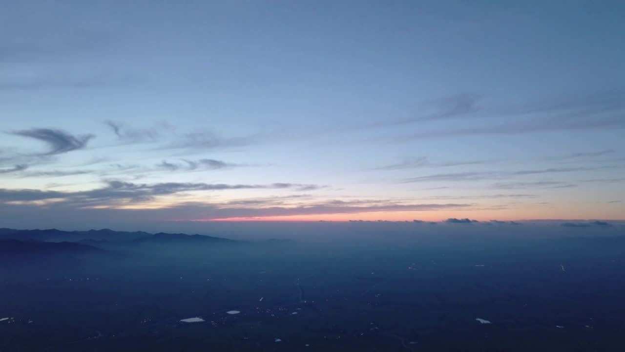 Atardecer al inicio del crepúsculo, horizonte con una banda rosada cambiante y nubes tenues desde un dron mostrando las luces del valle.