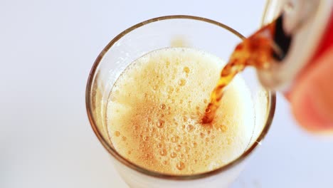 verter bebida de cola oscura en un vaso con hielo creando una cabeza espumosa con burbujas
