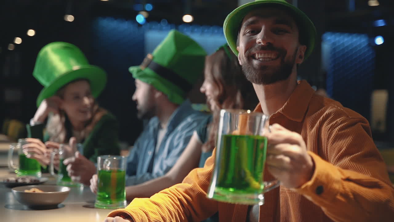 술집에서 성 패트릭의 날을 축하하는 친구들, 웃고 있는 행복한 남자는 카메라를 보고 맥주 한 잔으로 건배한다