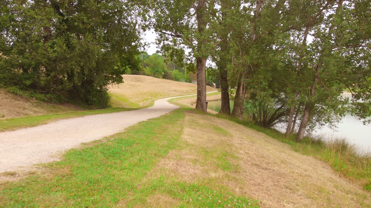 Discover the serene beauty of Lac de L'Orme Blanc near Toulouse, France. Tranquil turquoise waters, surrounded by lush trees and a winding pathway, offering a perfect escape into nature