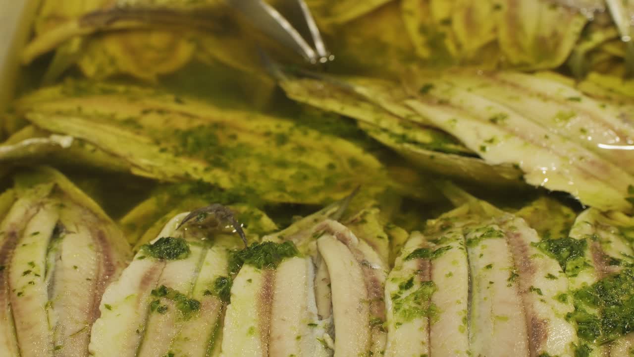 Delicious marinated fish fillets seasoned with herbs, submerged in olive oil, served in a white tray.