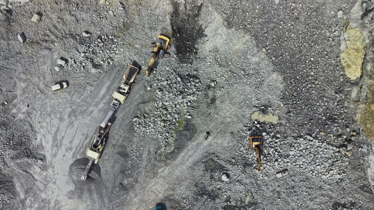 Granite quarry in operation with machinery and trucks moving materials in a rock-filled landscape during daylight hours