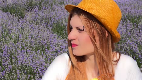 side profile headshot of young woman with eyebrow piercing and orange hat against lavender field, reflecting on life