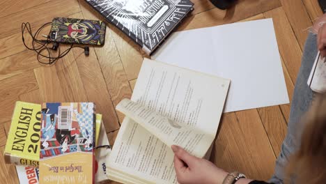 la niña se sienta en el suelo estudiando, pasando las páginas de un libro y tomando notas