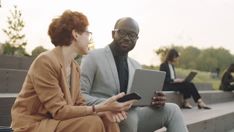 diverse colleagues using on laptop and having discussion outdoors