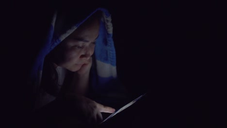 woman using smartphone under blanket