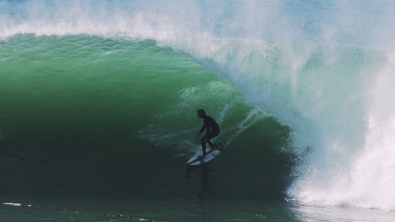 Surfer crouches into thick churning barrel with white foam trailing behind the wave