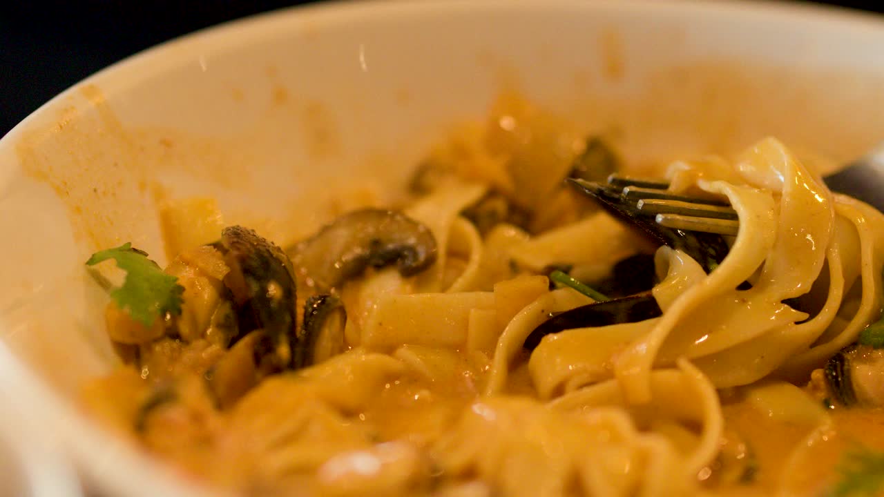 Close-up of fork twirling creamy seafood pasta with mussels, warm lighting, shallow depth of field