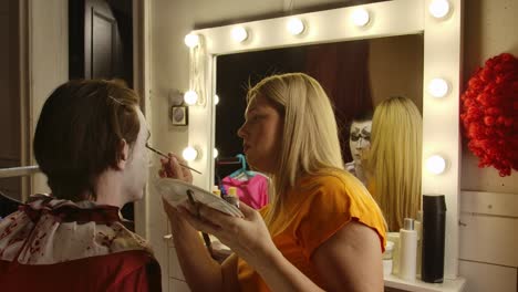 makeup artist applying special effects makeup to a person in a dressing room