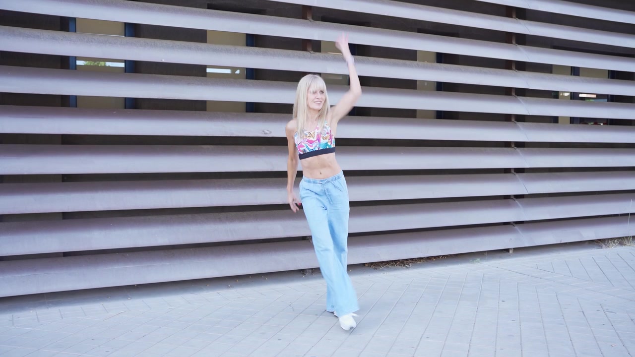 En dynamisk blond kvinde iført en farverig sports-bh danser i et pulserende bymiljø.