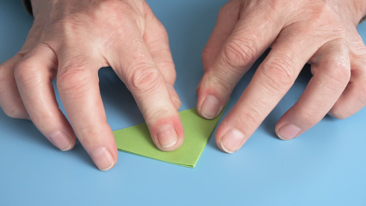 한 남자 가 초록색 종이 를 접어 오리가미 그림 을 만든다