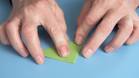 a man folds green paper to make an origami figure