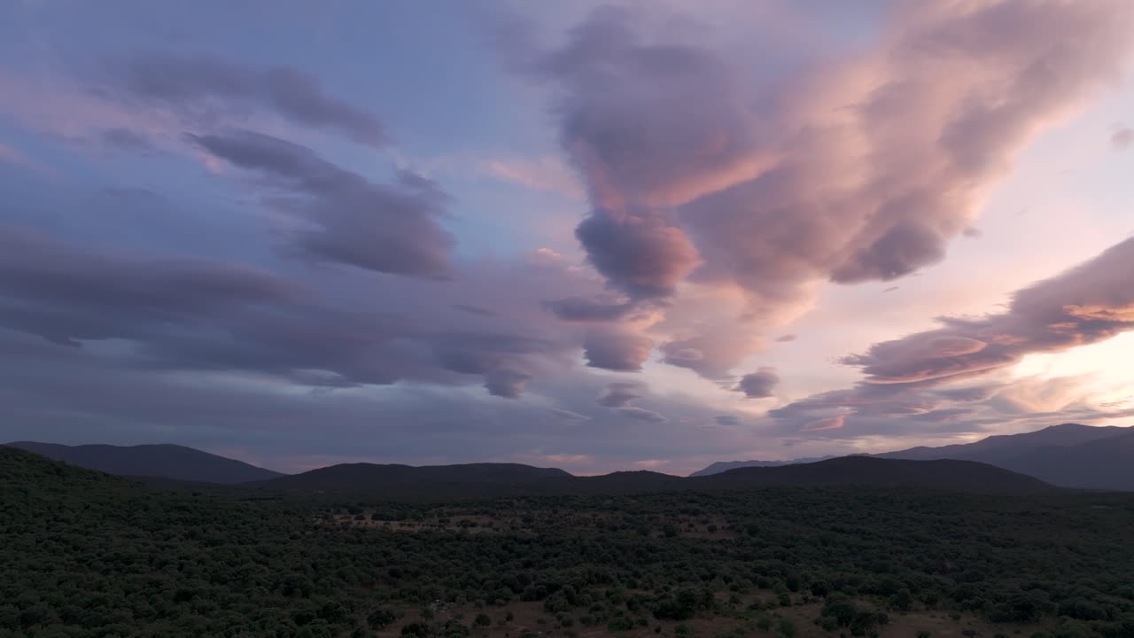 vuelo al atardecer y con un giro de la cámara vemos un valle con sus exuberantes bosques con un cielo espectacular con nubes alargadas que van de azul a naranja, estas montañas toman un tono azul oscuro