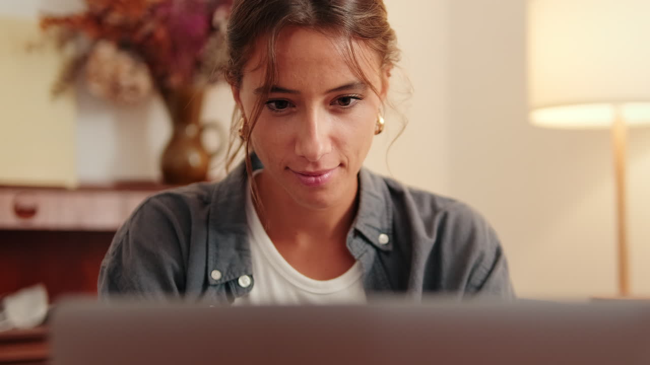 Ung kvinde smiler, mens hun bruger bærbar computer derhjemme