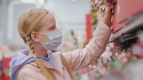 a child in a protective mask chooses christmas tree toys in the store. shopping during the pandemic