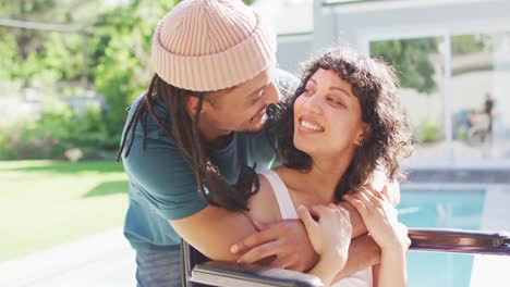 feliz mujer biracial en silla de ruedas abrazando y besando con pareja masculina con rastas en el jardín