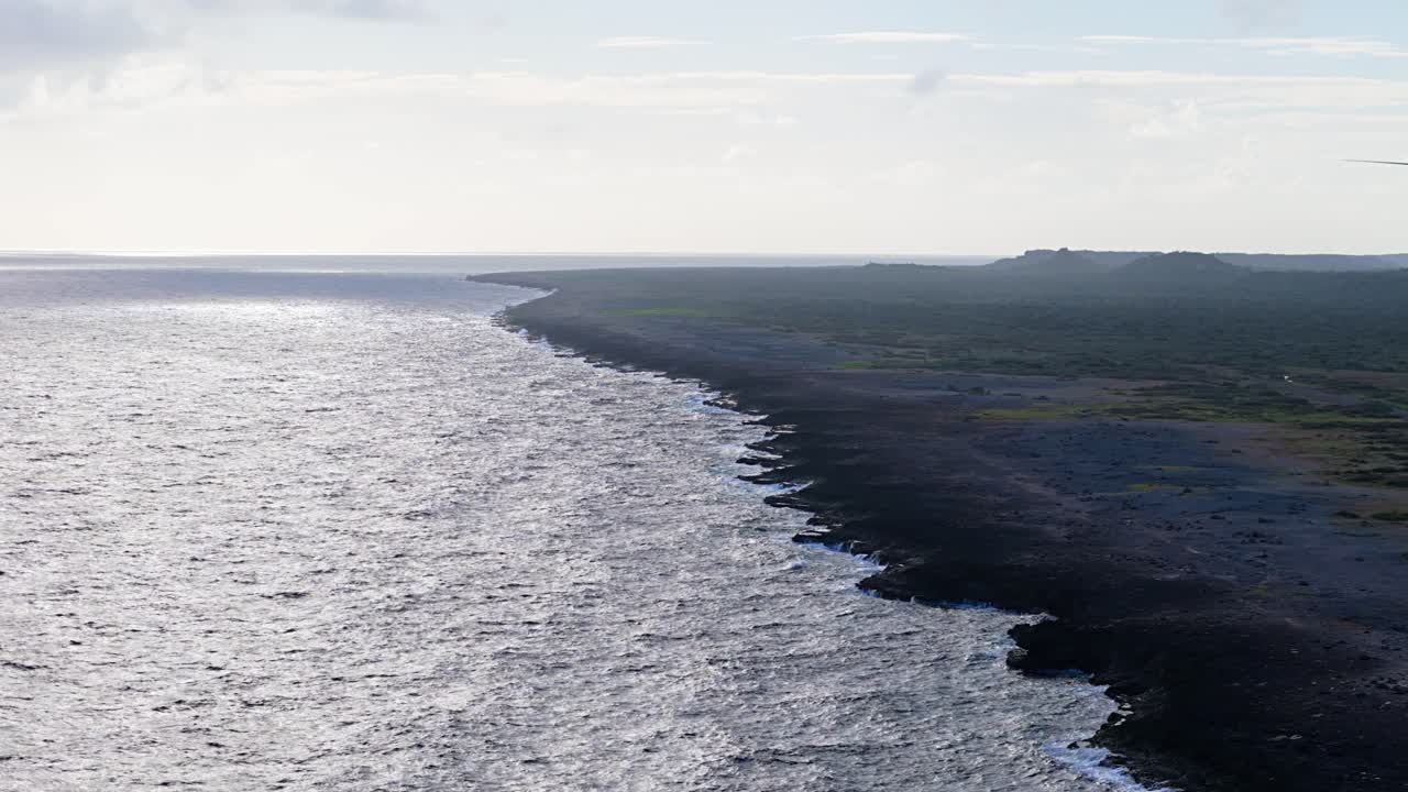 pan de camiones aéreos a través de la roca volcánica negra que se extiende en el agua del océano abierto