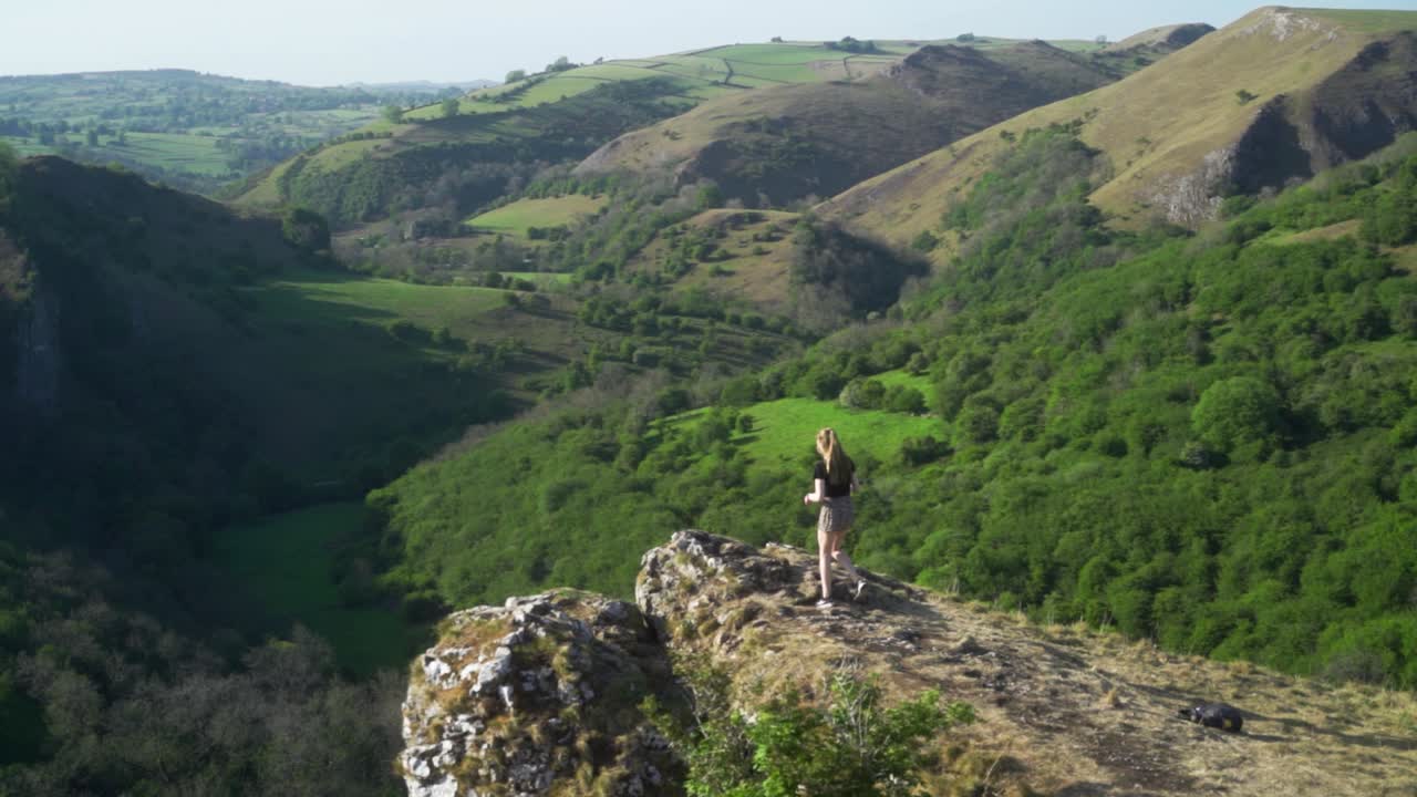 토르의 동굴, 애쉬본, 피크 디스트릭트, 잉글랜드 위의 절벽 가장자리를 향해 걸어가는 젊은 금발 여성의 느린 동작