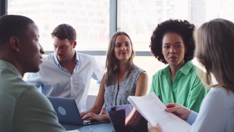 Multi-Cultural-Business-Team-Meeting-Around-Office-Boardroom-Table-With-Laptops-Discussing-Documents