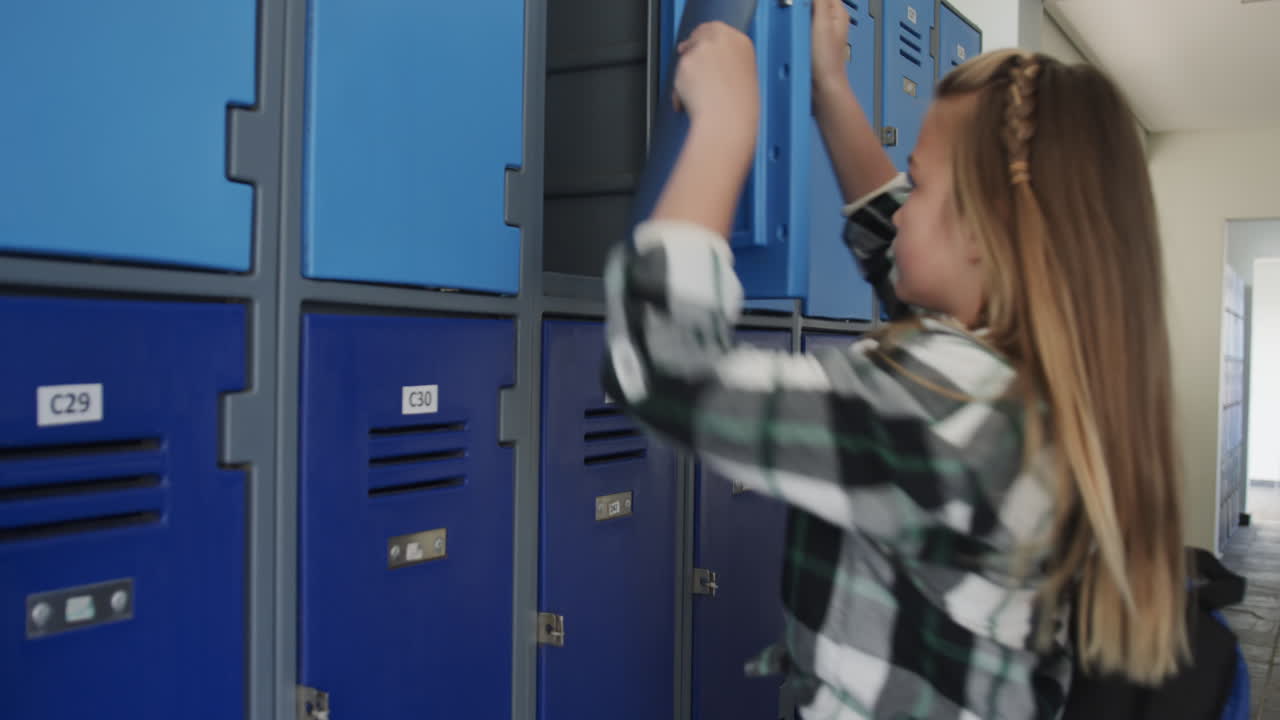 In school, young girl reading folder in hallway near lockers, concentrating