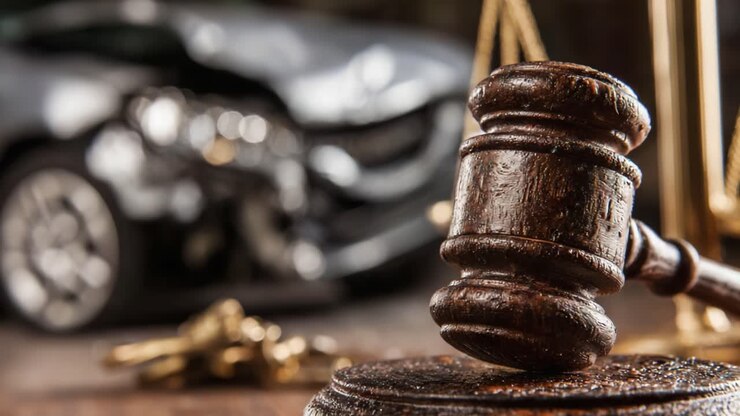 Un martelletto posto in primo piano, giustapposto allo sfondo sfocato di un incidente automobilistico, che illustra l'intersezione tra diritto e lesioni personali.