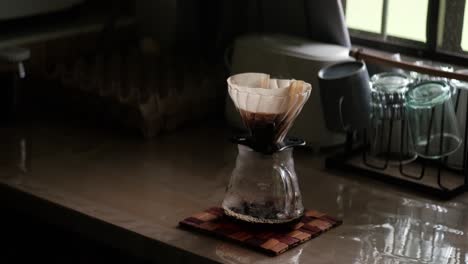 brewed coffee dripping into glass carafe through pour-over filter paper and v60 on kitchen countertop - medium static shot