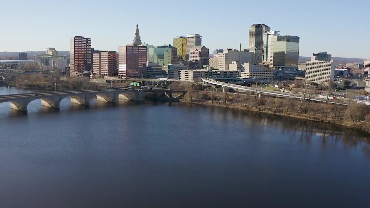 Riprese aeree con drone del paesaggio urbano del centro di Hartford che si eleva sopra il fiume, volando verso uno svincolo stradale