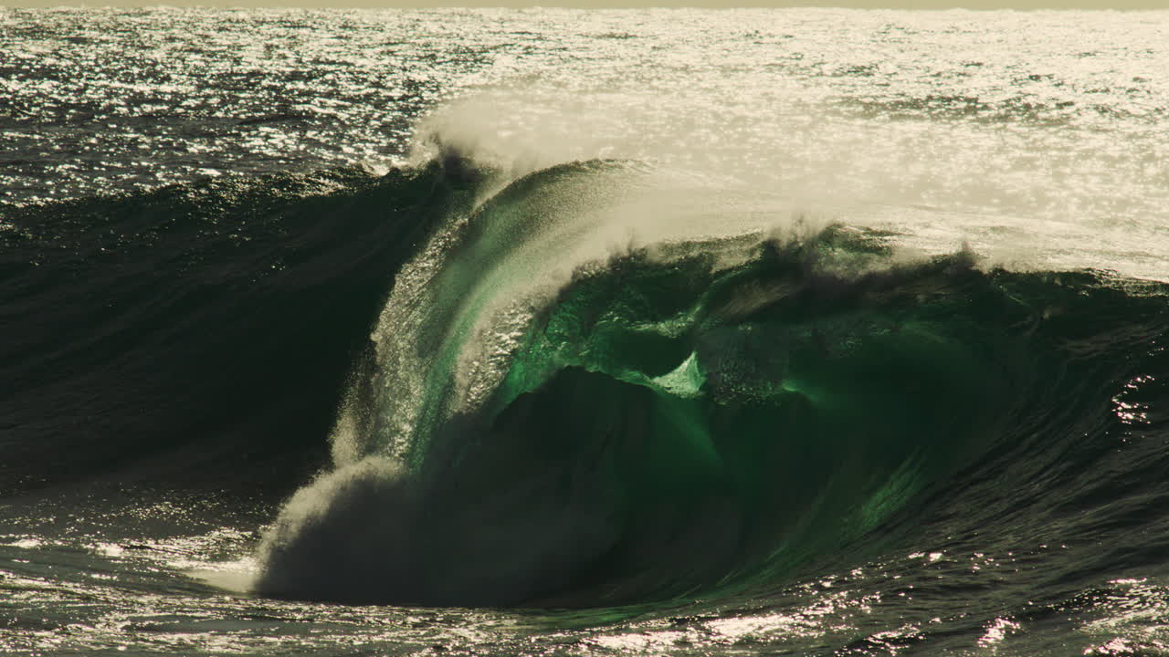 Mid curl wave barrels with white mist illuminated by soft light over textured ocean surface