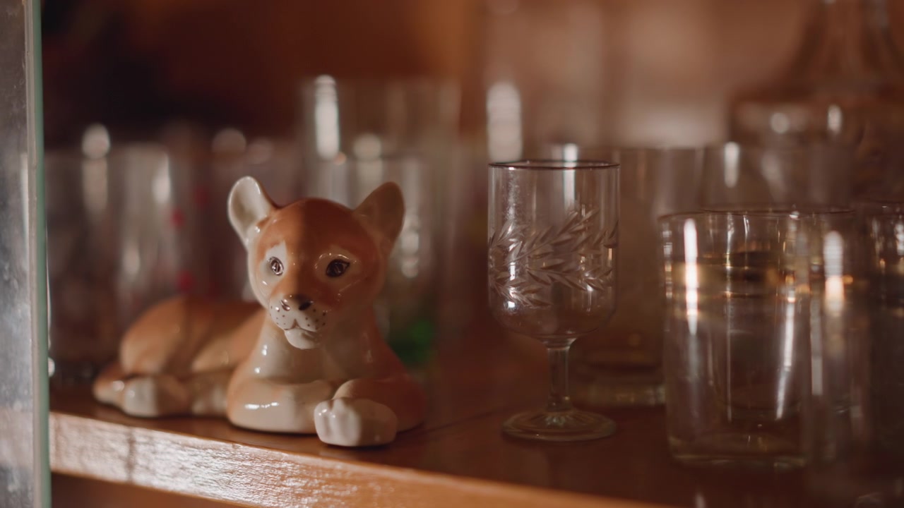 Warm close up glass ceramic fox on wooden shelf, collector display of vintage goblets and cups, soft bokeh and golden reflections, cozy nostalgic atmosphere with dusty patina and delicate etched