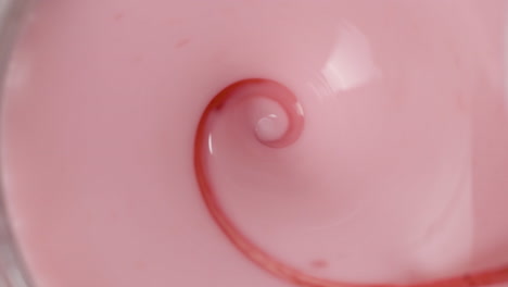 hypnotizing rotation of a strawberry milkshake with a thin stream of syrup, viewed from above