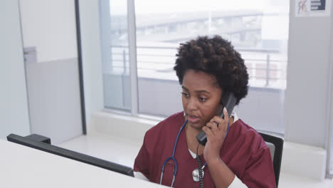 African-american-female-doctor-talking-on-phone-in-hospital,-slow-motion