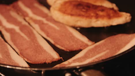 vegan bacon cooking in hot frying pan next to plantbased chicken fillets