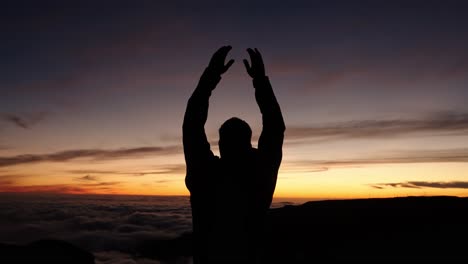silhouette of a man raising both arms in the air while watching the sunset at pico do arieiro, madeira, portugal.