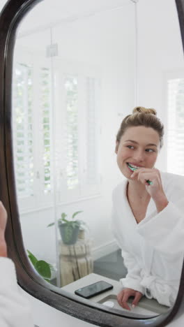 vertical video of biracial woman brushing teeth looking in mirror in bathroom, slow motion