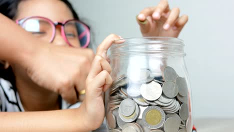 asian little girl putting the coin in to a glass jar shallow depth of field select focus on jar