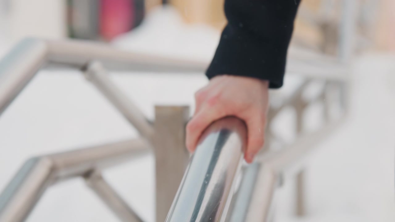Close-up tangan seseorang menyentuh dan menjelajahi pagar logam yang dingin dalam cuaca dingin. Fokus tetap pada interaksi taktil antara jari, detail tekstur es seperti pola embun beku atau air.