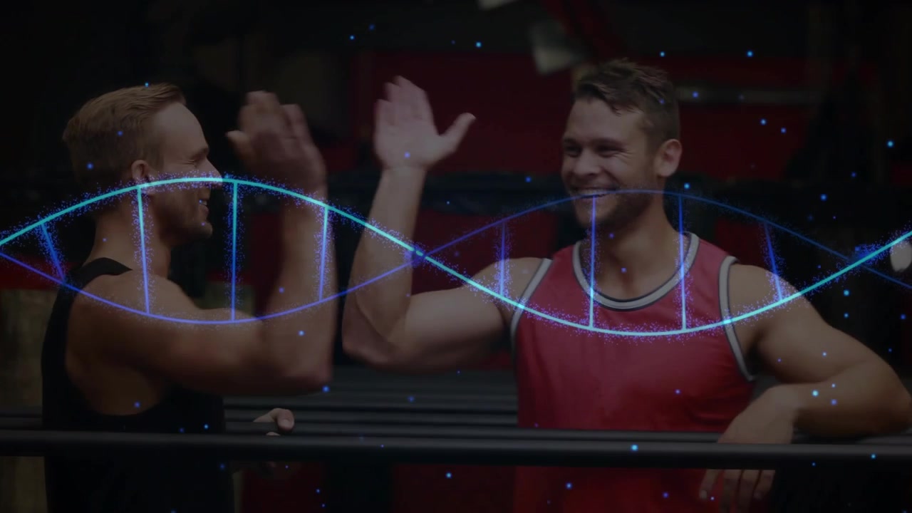 Ein Spotter stützt die Beine des Sportlers, überprüft die Haltung, während der Sportler einen L-Sitz hält und Partner unter einer Helix jubeln.