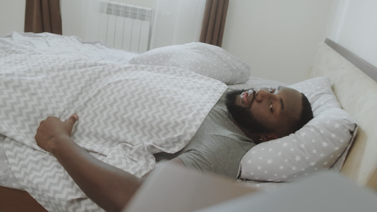African man slowly waking up in morning. Young male person oversleep in morning.