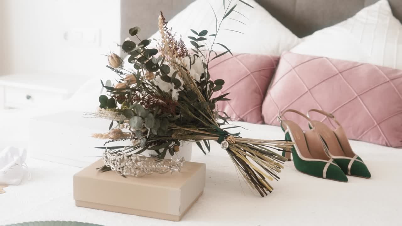 fotografía de cerca de los accesorios femeninos de la boda en la cama, ramos de flores, tacones altos y una tiara