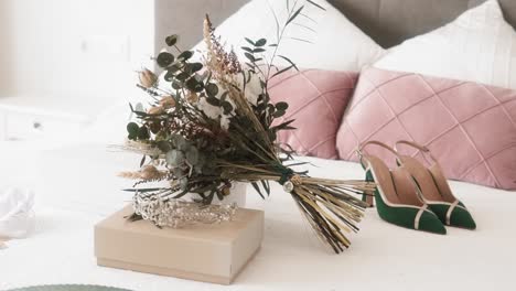 fotografía de cerca de los accesorios femeninos de la boda en la cama, ramos de flores, tacones altos y una tiara