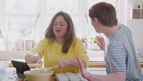 Una-Pareja-Joven-Con-Síndrome-De-Down-Poniendo-La-Mezcla-En-Cajas-De-Papel-Para-Cupcakes-En-La-Cocina-De-Casa