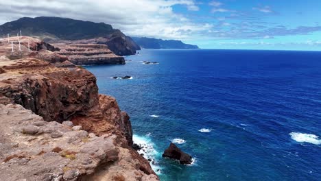 wind turbines at the edge of the clifftop near miradouro da ponta do rosto with couple tourists in east madeira, portugal