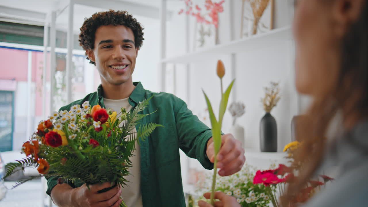 Fröhlicher Kunde überreicht der Verkäuferin im Pflanzengeschäft eine Blume. Romantisches Konzept.