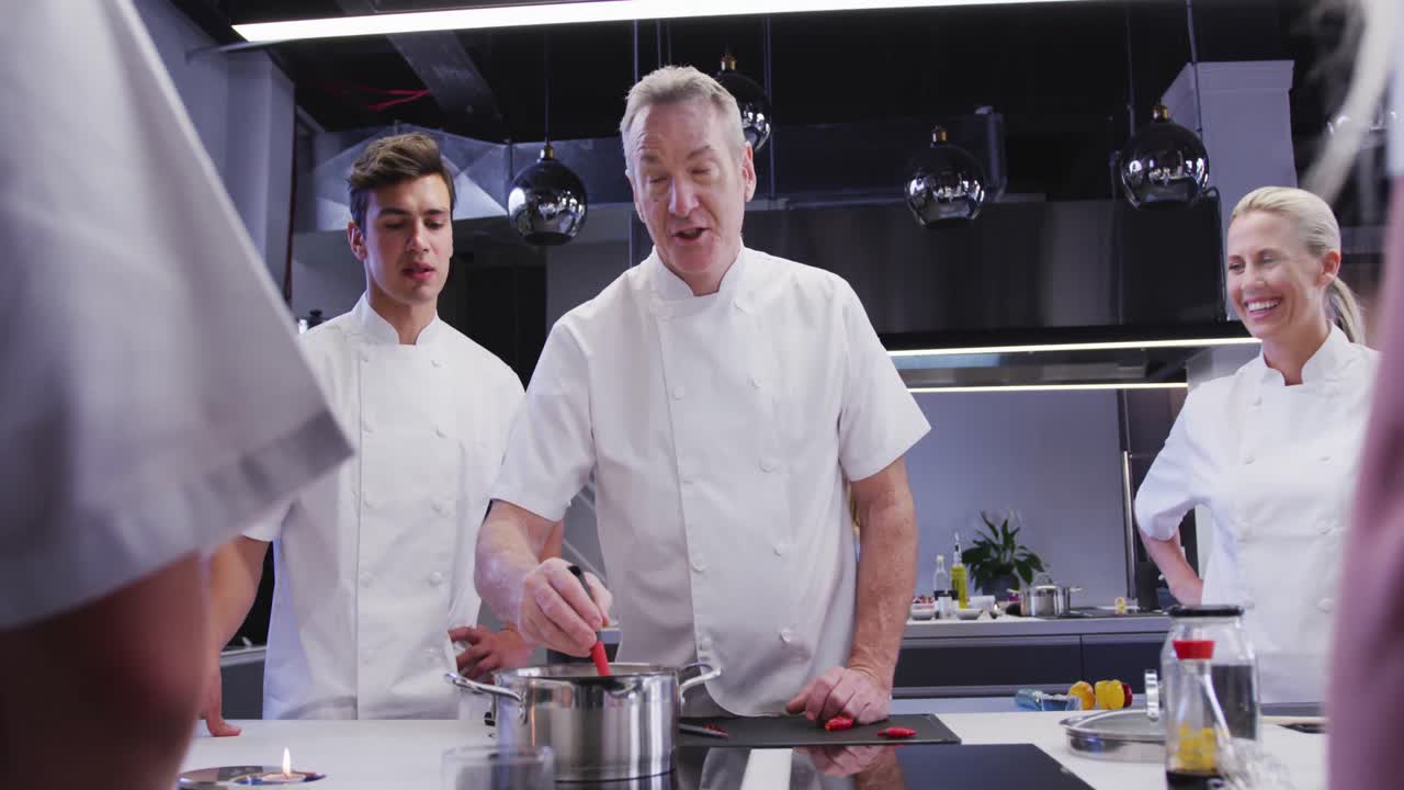 cocinero caucásico profesional en una cocina de un restaurante que enseña a un grupo de chefs aprendices