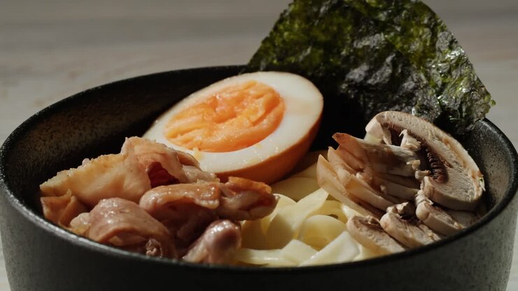 Mano che aggiunge cipollotti a una ciotola di ramen