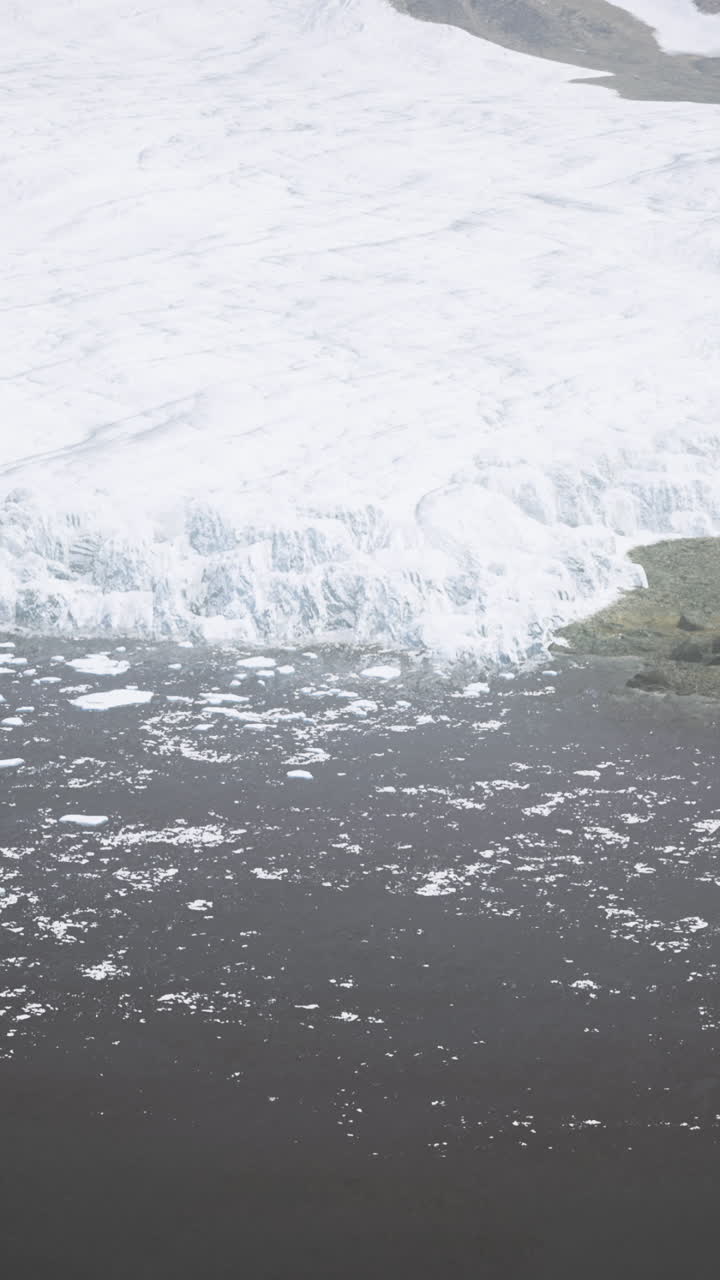 Glacier melting into dark water body with rocky landscape in background