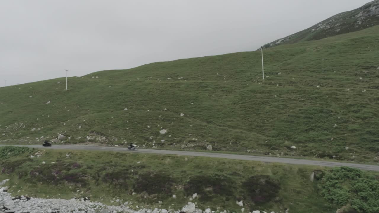 Drone panning shot of two motorbikes riding along the coastal road along the Scotland North Coast 500 route