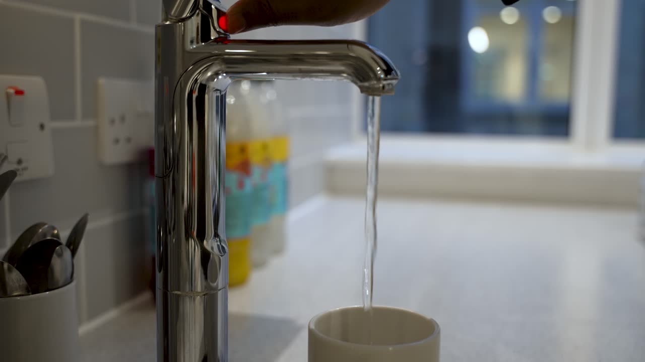 una persona toma un sorbo refrescante de agua directamente de un grifo en una taza