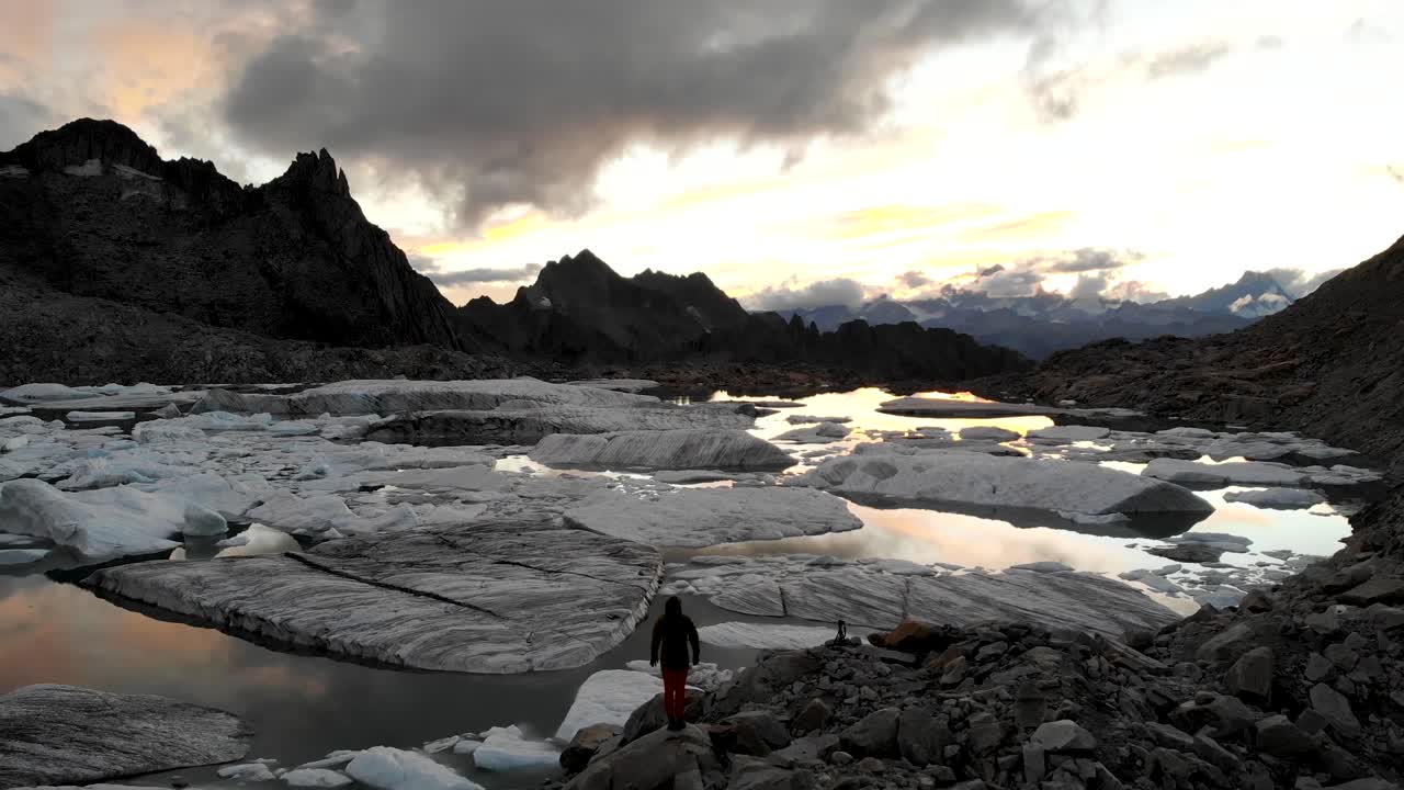 vista aérea de un excursionista mirando un lago glaciar lleno de icebergs derretidos en partes remotas de los alpes suizos con el brillo de la puesta de sol reflejado en el agua