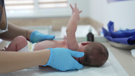 little baby in a diaper lying on a pediatrician's table. neonatologist's hands in blue gloves are taking child and turn it backwards.